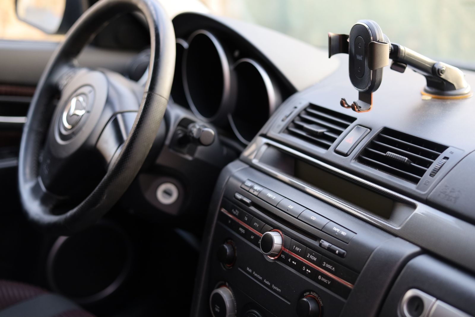 Close-up of a car dashboard and steering wheel area with a black cellphone holder mounted on it