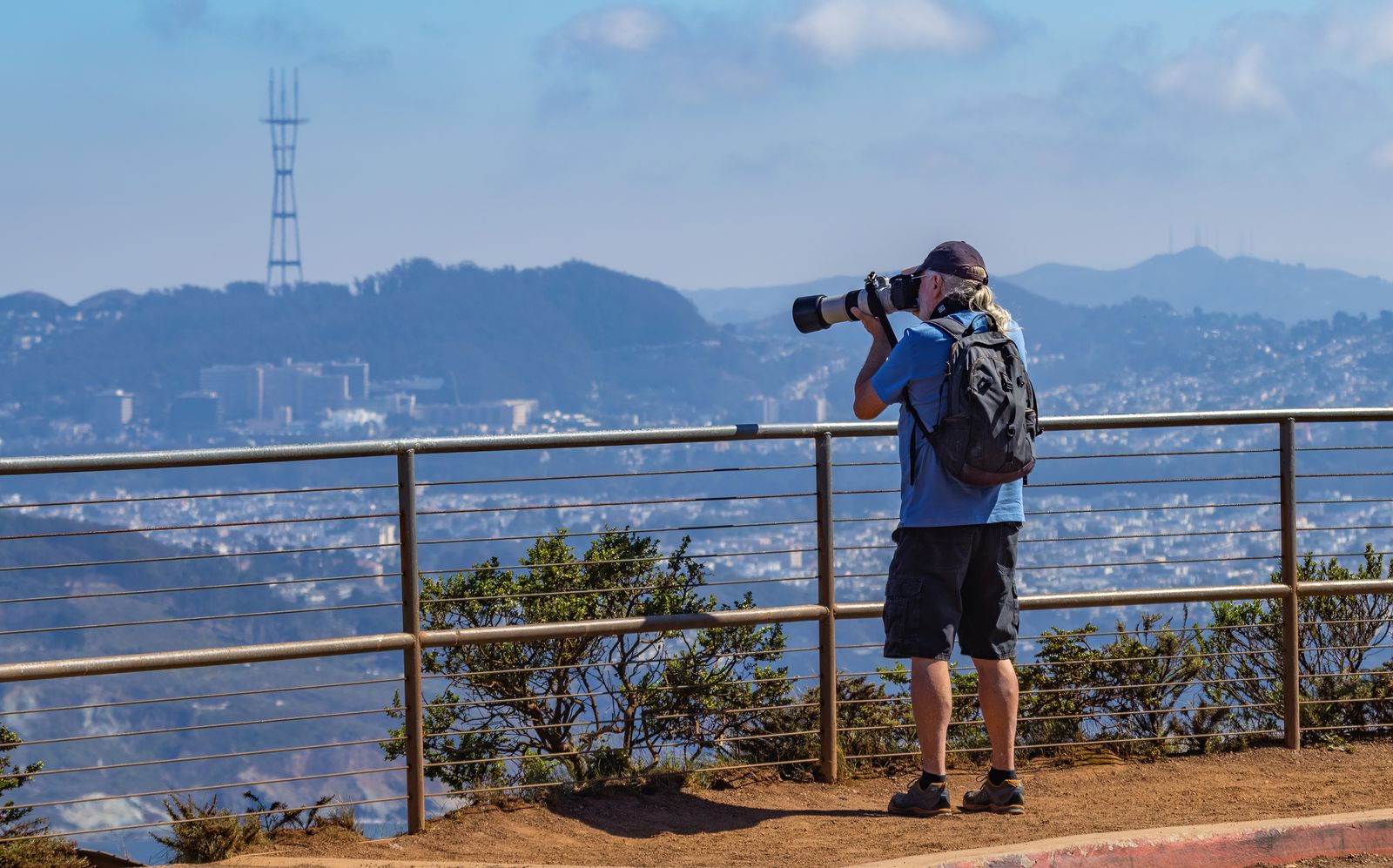 Traveler with a backpack standing on a view deck using a camera