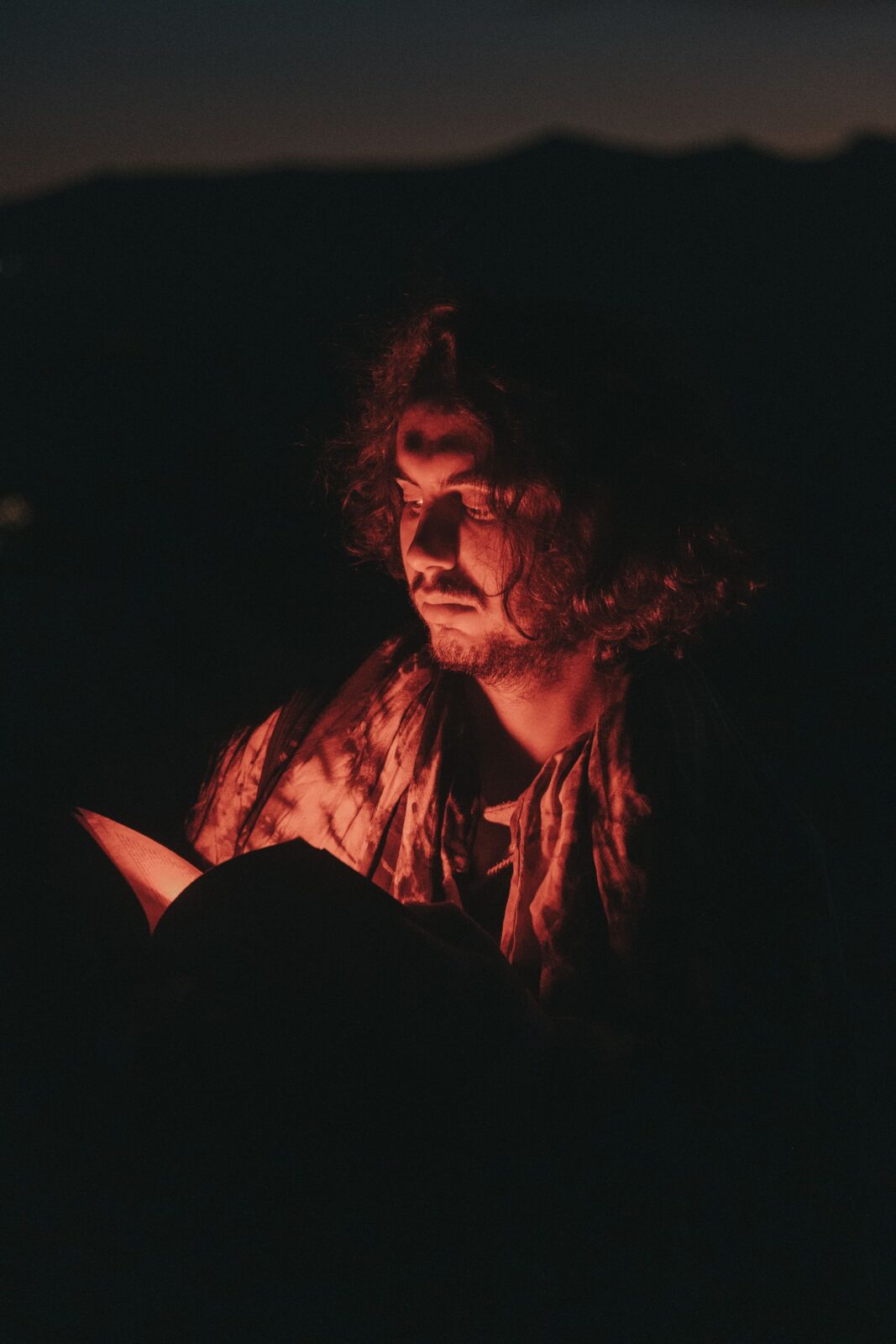 A person reading an open book lit by a small warm light in a dark room