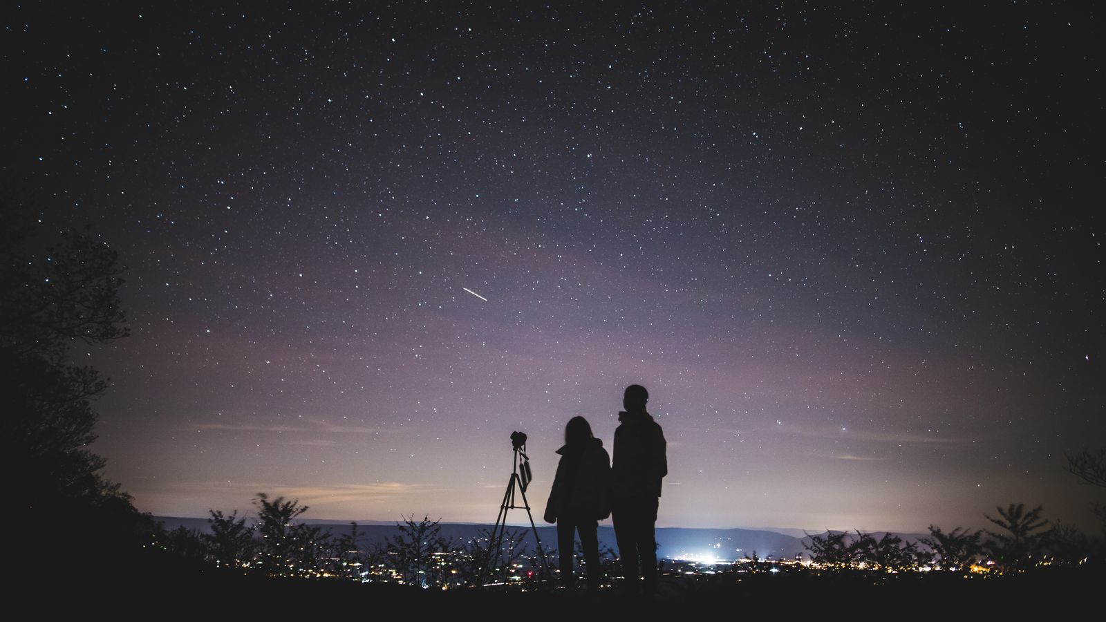 Silhouette of two people stargazing together under a starry night sky