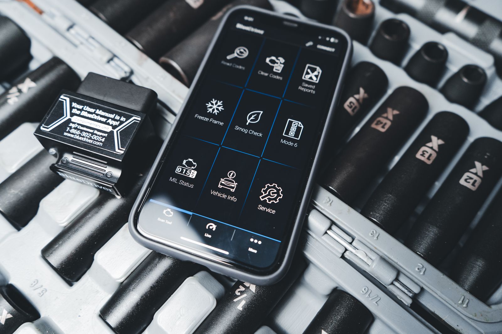 Smartphone running a car diagnostic app next to an OBD2 scanner in a garage