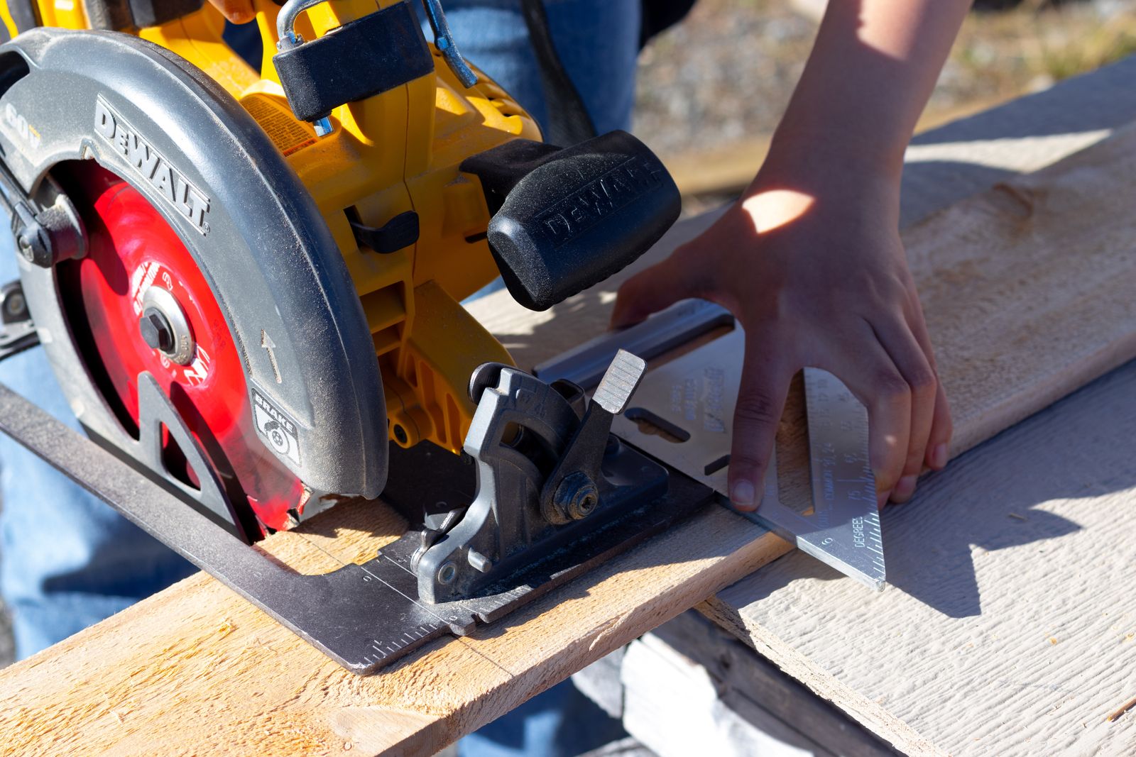 Cutting a wooden board using a circular saw guided by a speed square