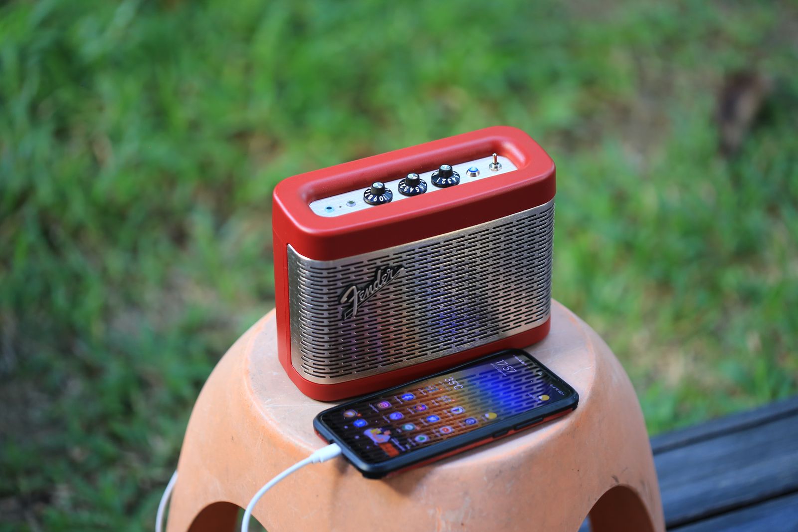 A portable Bluetooth speaker and phone on a stool outdoors in nature