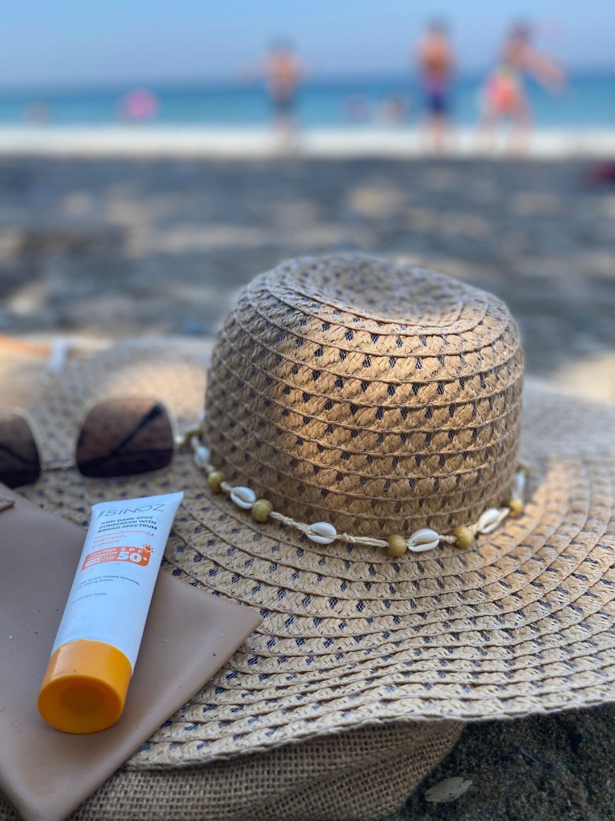 Straw hat and a bottle of sunscreen resting on sand at the beach