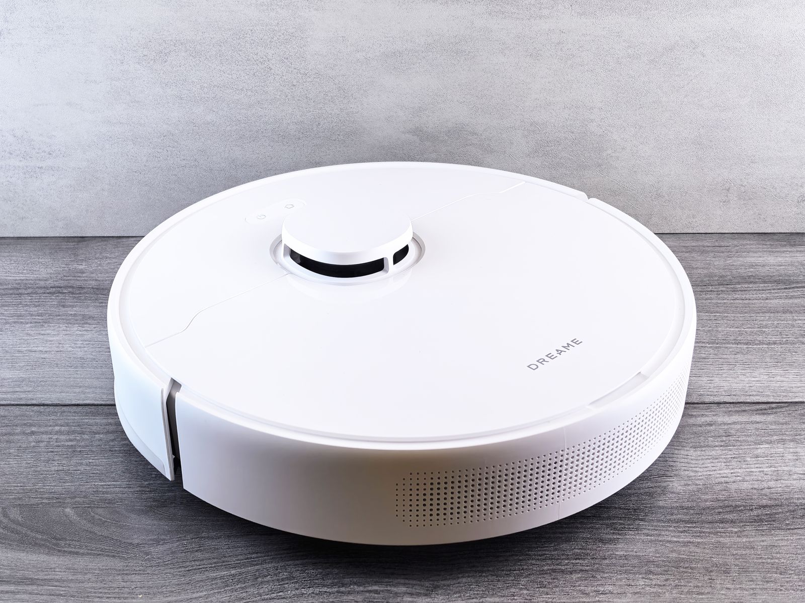 A sleek round robot vacuum cleaning a hardwood living room floor in daylight