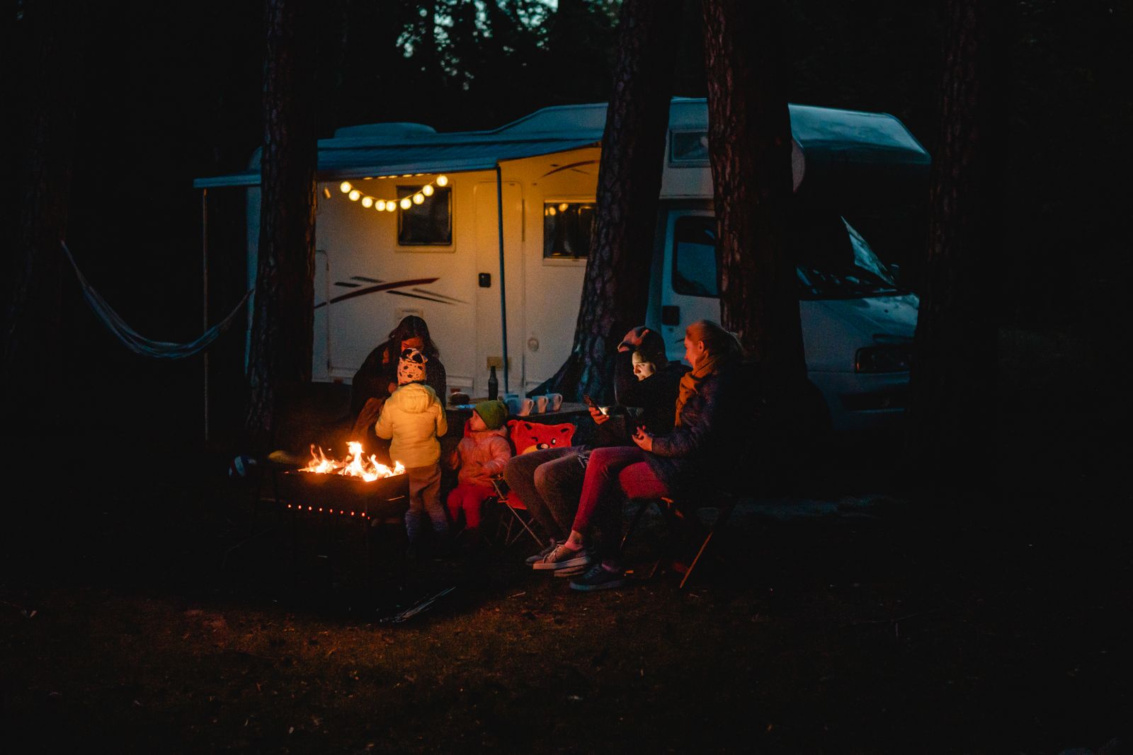 People sitting on camping chairs near a fire at night