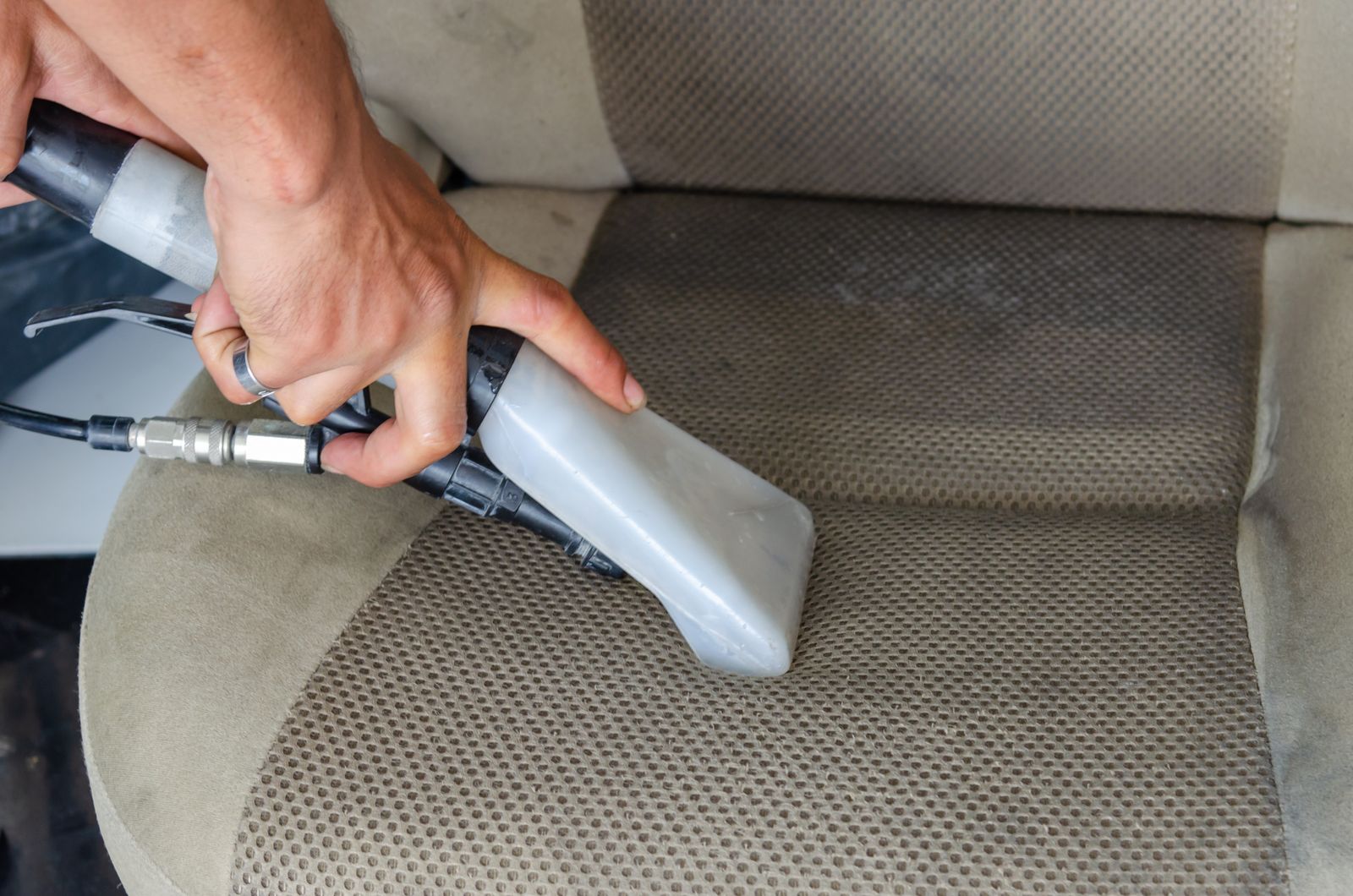 Person using a handheld vacuum to clean a car interior seat and carpet