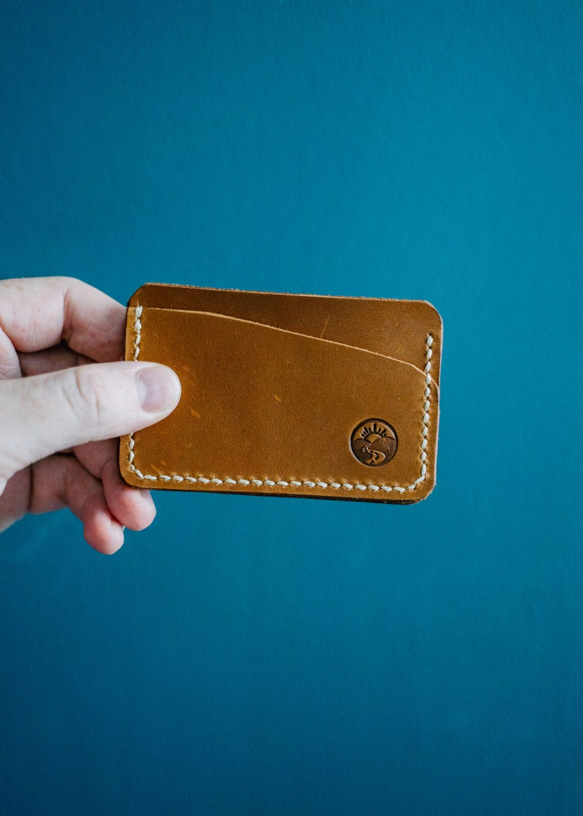 A hand holding a slim brown leather wallet