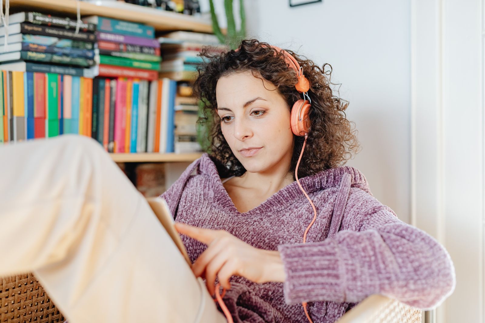 Person in a cozy sweater listening to headphones at home while holding a physical book