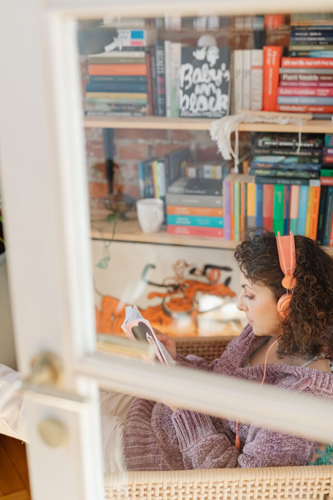 Woman relaxing at home listening to an audiobook through headphones near a bookshelf
