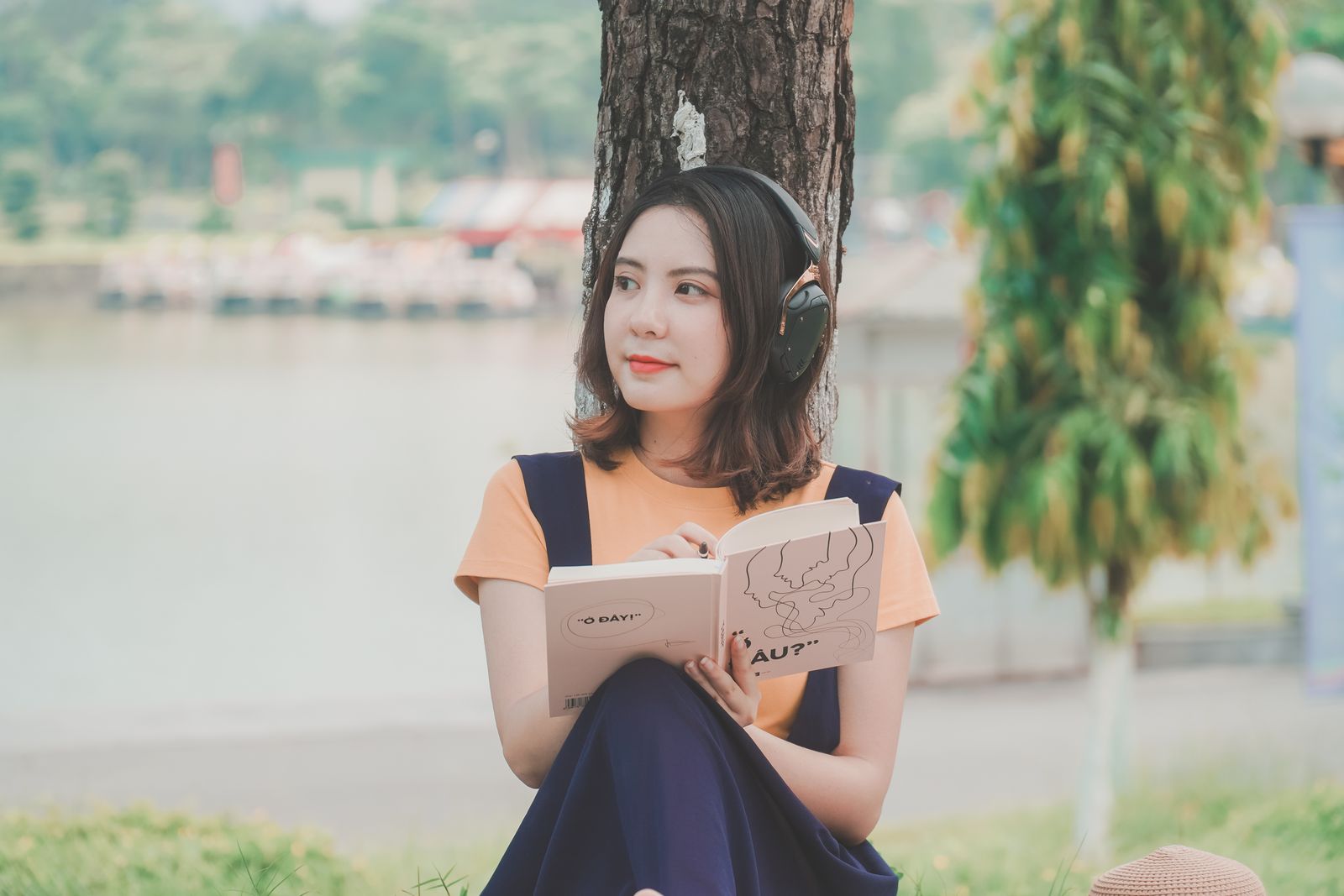 Person sitting outdoors under a tree enjoying music and a book together