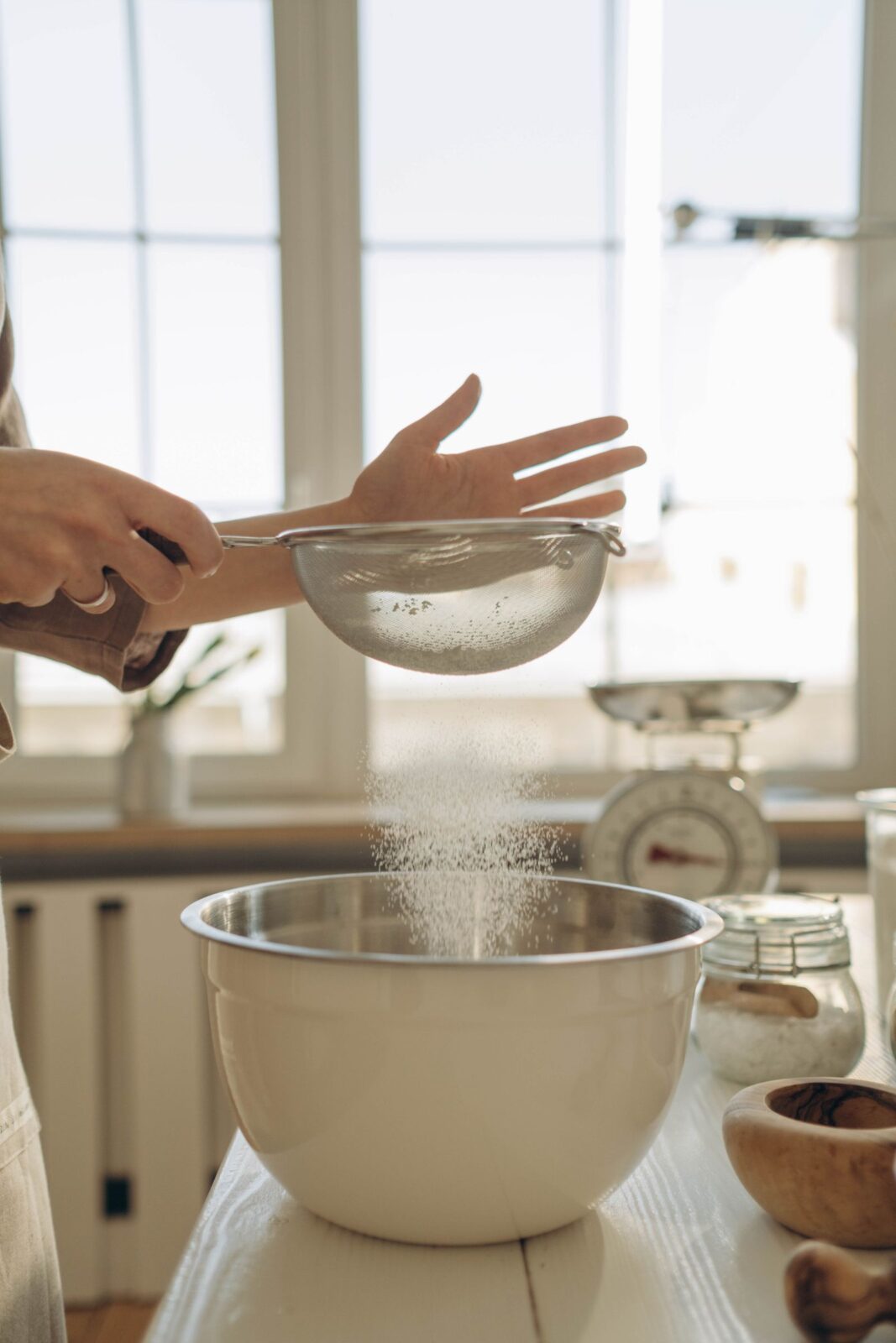 A person sifting flour into a bowl while baking
