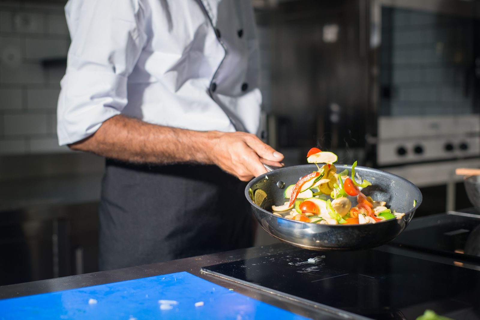 Chef cooking fresh vegetables in a frying pan