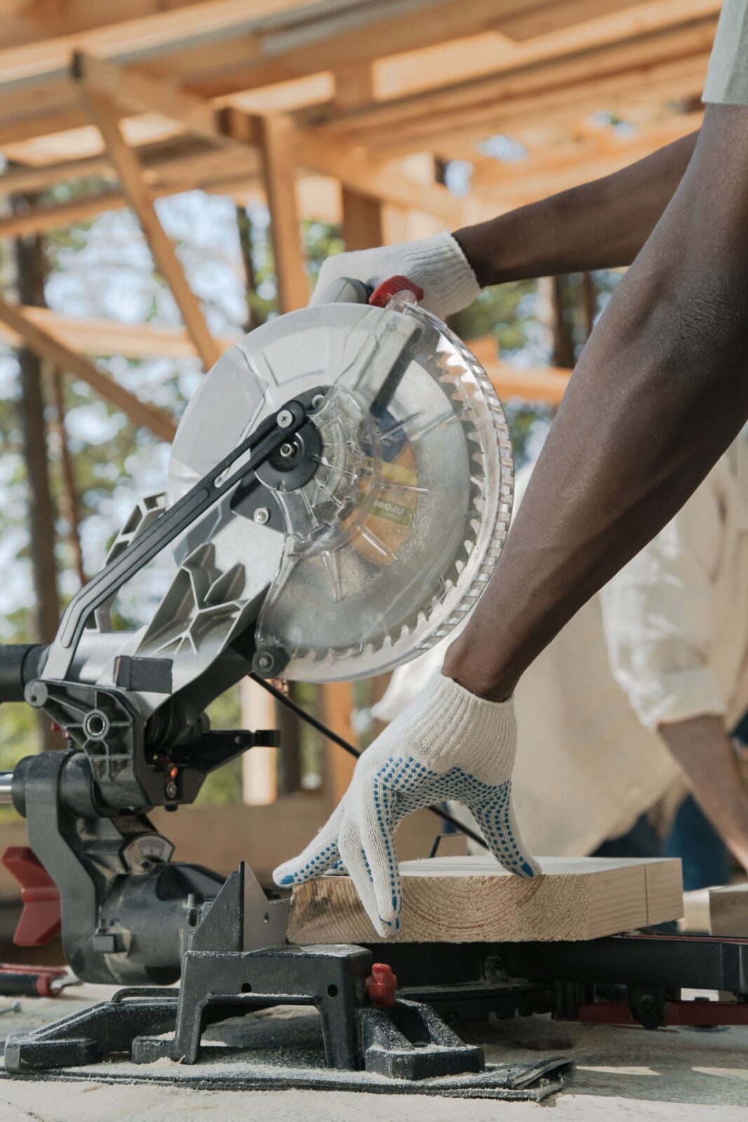 Person using a cordless circular saw to cut a wood board outdoors, wearing safety gloves
