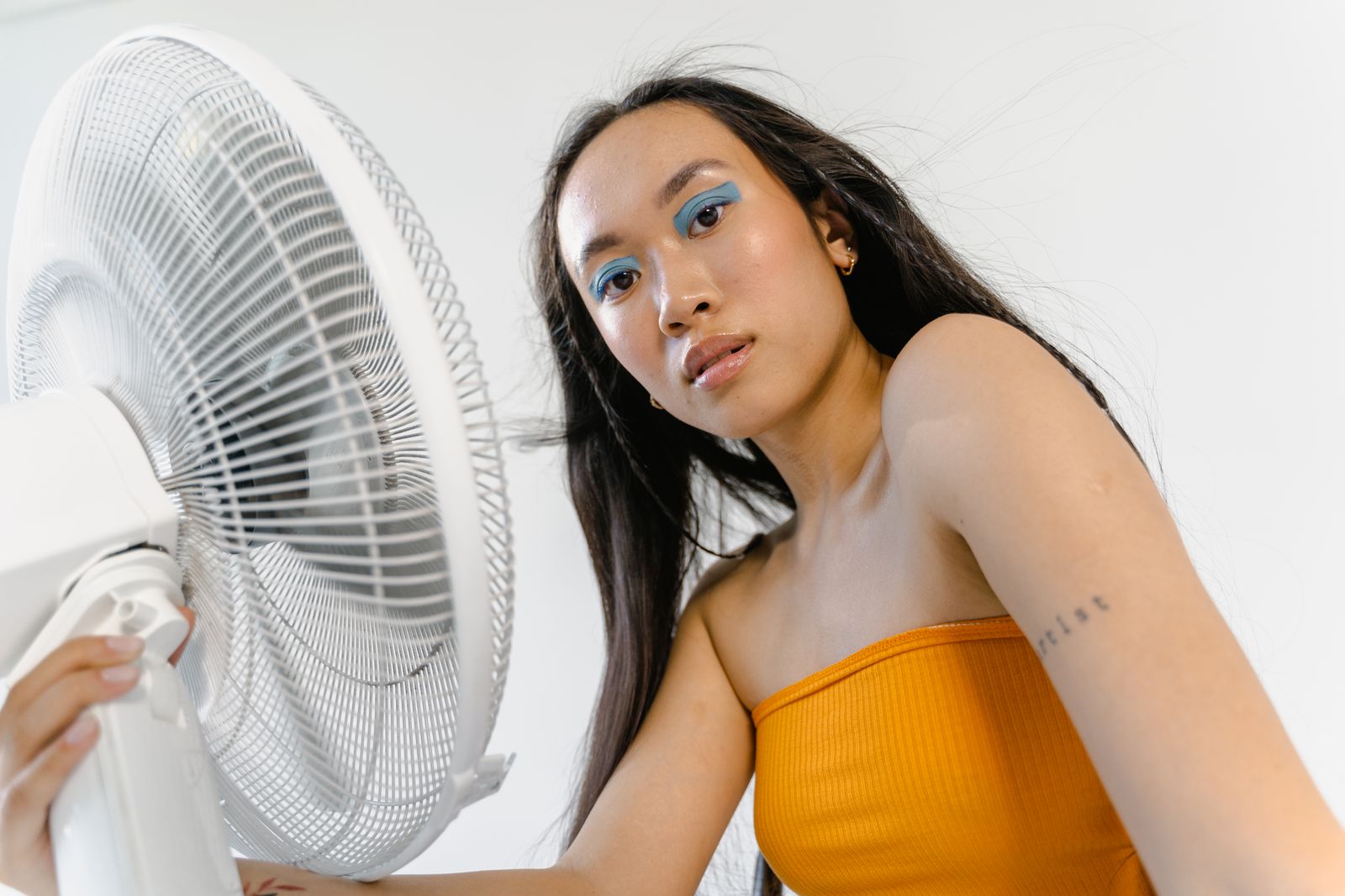 Woman cooling off in front of an electric fan indoors on a hot summer day