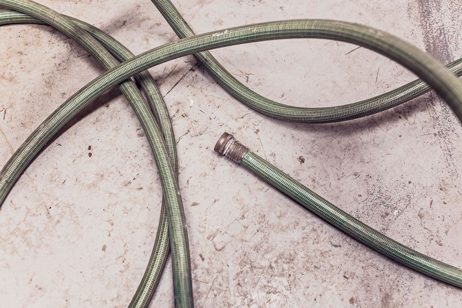 Coiled green garden hose lying on a concrete surface