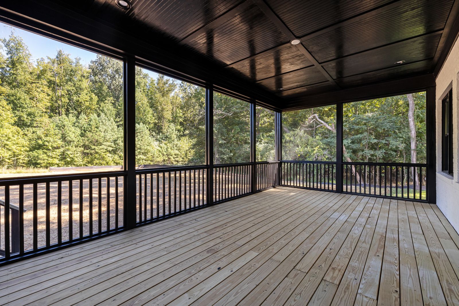 Newly constructed screened-in porch with light wood floor, dark posts and railings, overlooking a yard