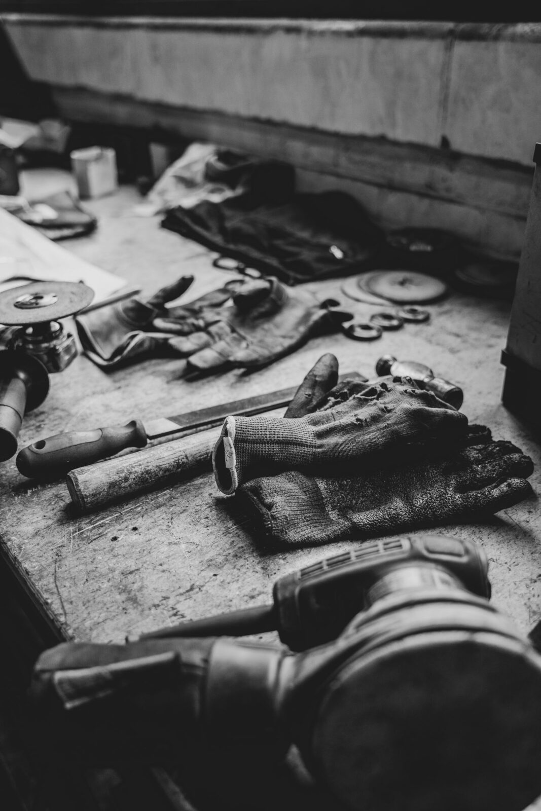 Black and white photo of a cluttered wooden workbench with hand tools and gloves