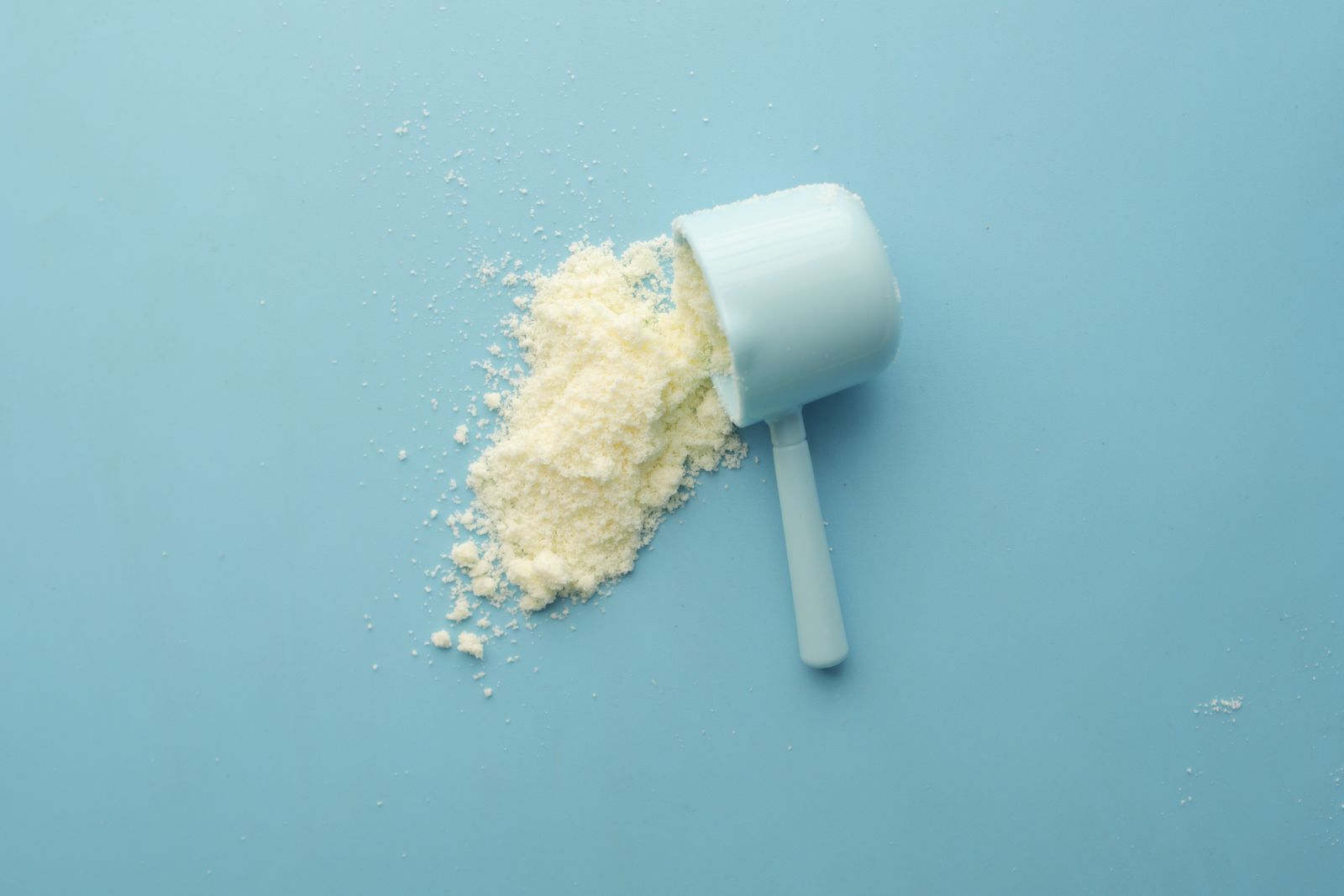 Scoop of white collagen powder spilling onto a bright blue background
