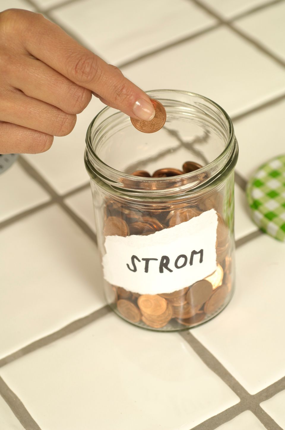 Hand placing a coin into a clear glass jar on a kitchen countertop