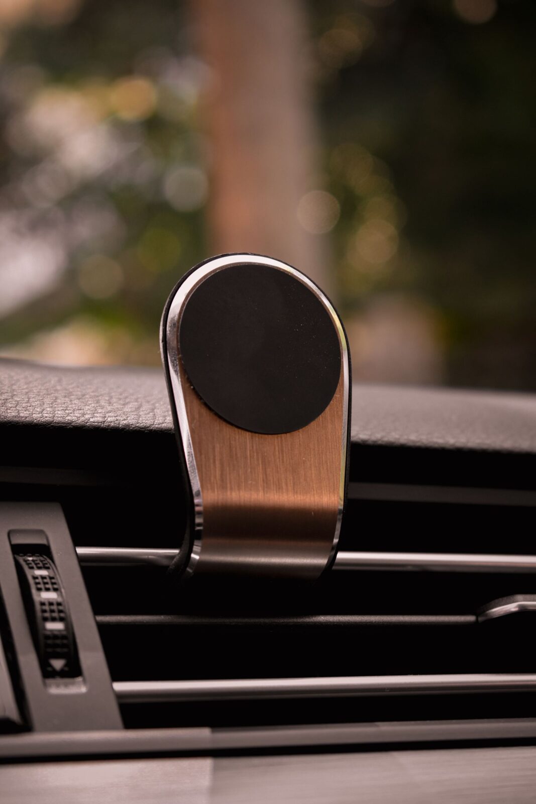 A magnetic phone mount clipped onto the horizontal louvers of a car's air conditioning vent, without a phone attached