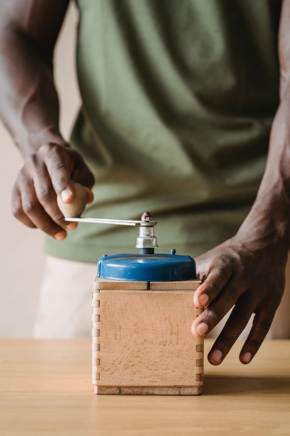 Close-up of hands operating a vintage-style manual coffee grinder on a wooden table