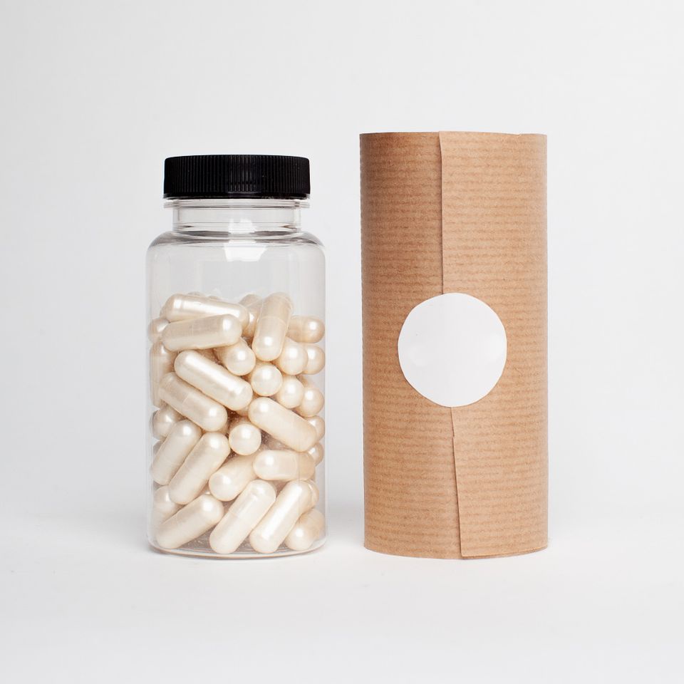 Clear plastic bottle filled with white supplement capsules next to kraft paper packaging