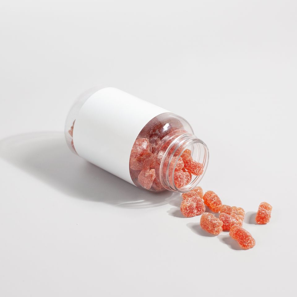 Colorful supplement gummies spilled from an unlabeled clear bottle on a white surface