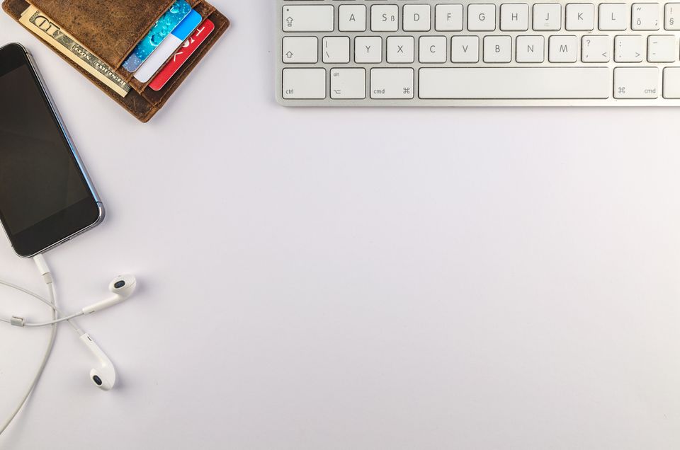 Overhead flat lay of a smartphone, keyboard, earphones, and a slim wallet arranged on a desk
