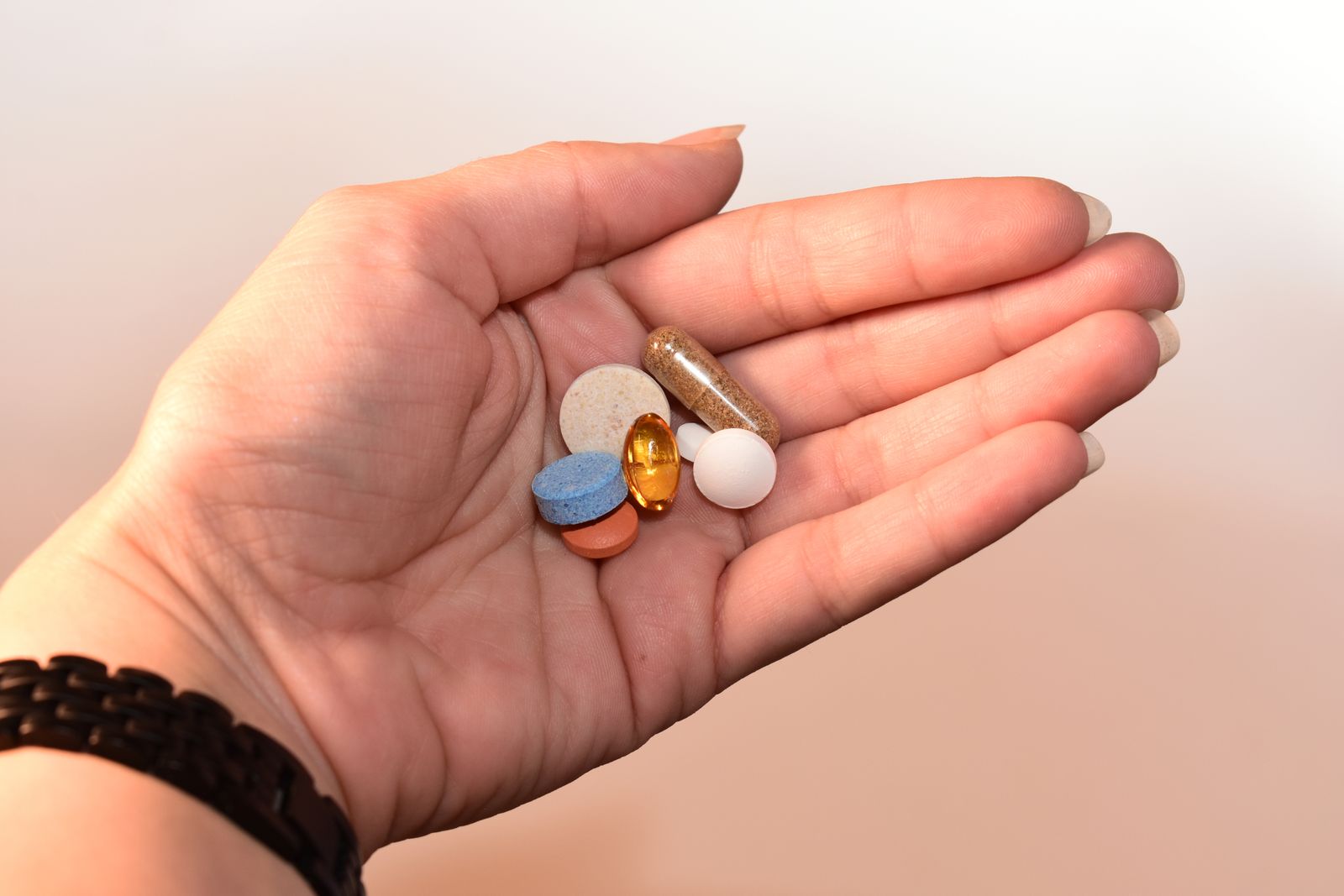 Close-up of a hand holding a variety of colorful dietary supplement capsules
