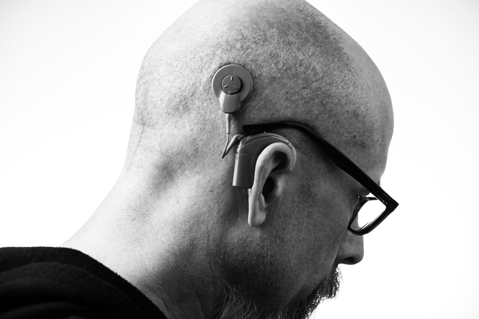 Studio portrait of a man wearing glasses and a behind-the-ear hearing aid