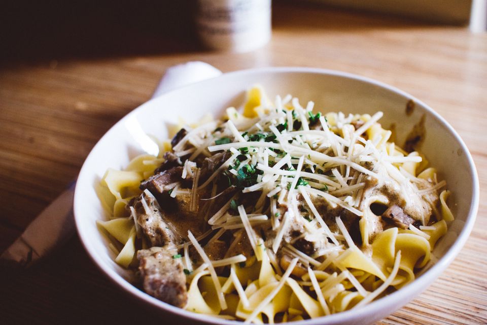 Close-up of pasta with creamy mushroom sauce and herbs in a bowl on a wooden table