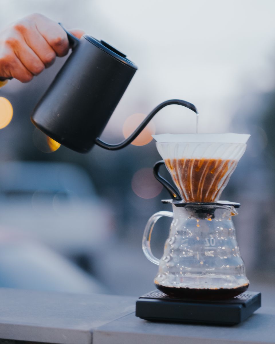 Person pouring hot water from a kettle over a V60-style pour-over coffee dripper
