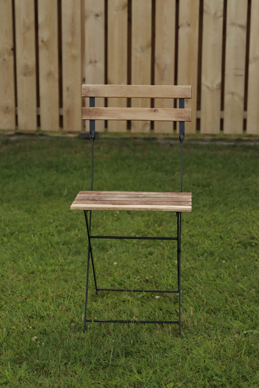 A folding wooden-slat outdoor chair set up on a grass lawn in front of a fence