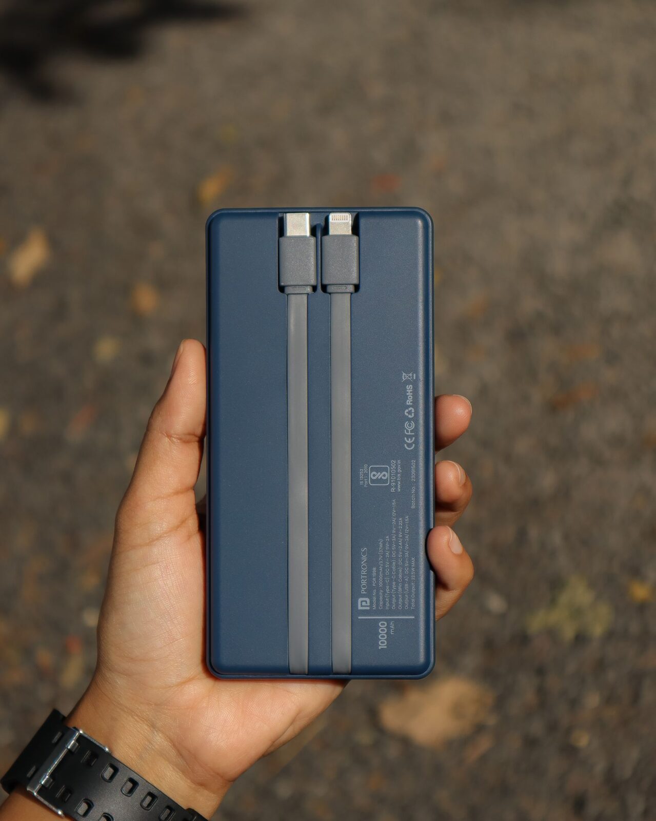 A person holding a compact portable power bank with USB cables, outdoors in daylight