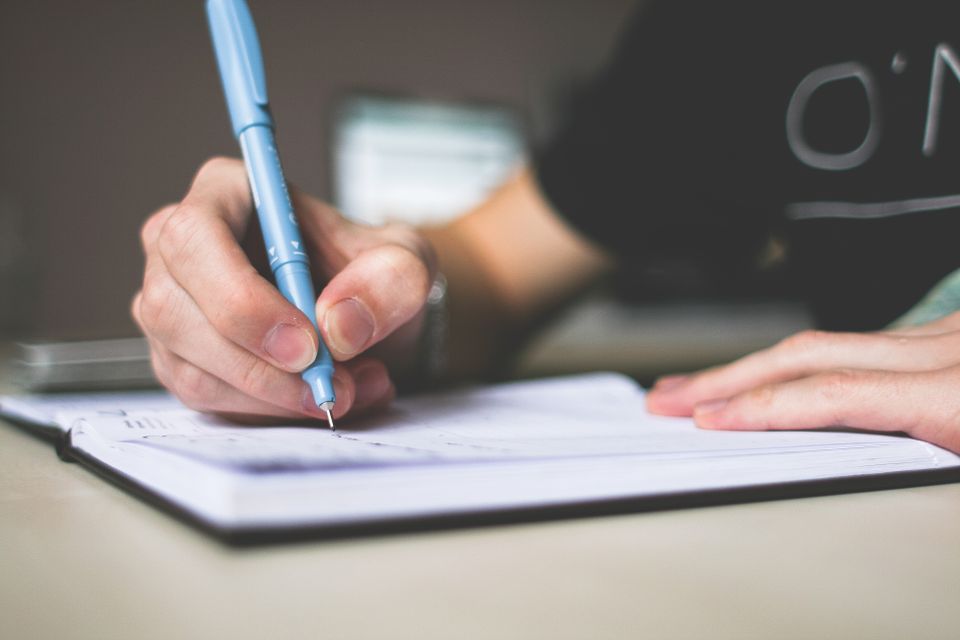 Close-up of a hand holding a blue pen while writing in a notebook