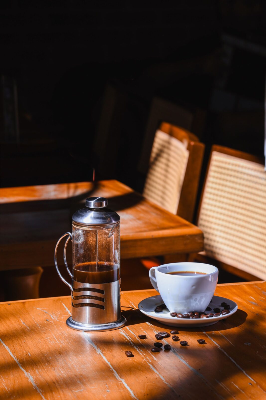 A French press and coffee cup on a sunlit wooden table