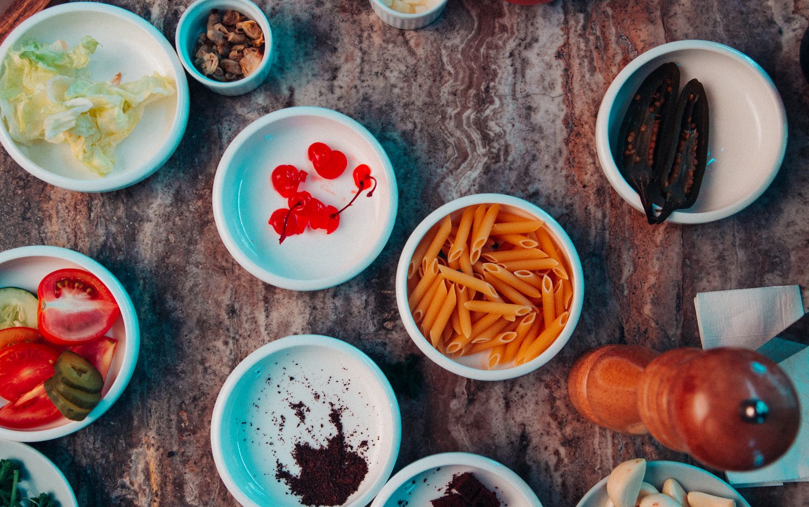 Overhead view of bowls with pasta, garlic, herbs, and vegetables arranged for cooking