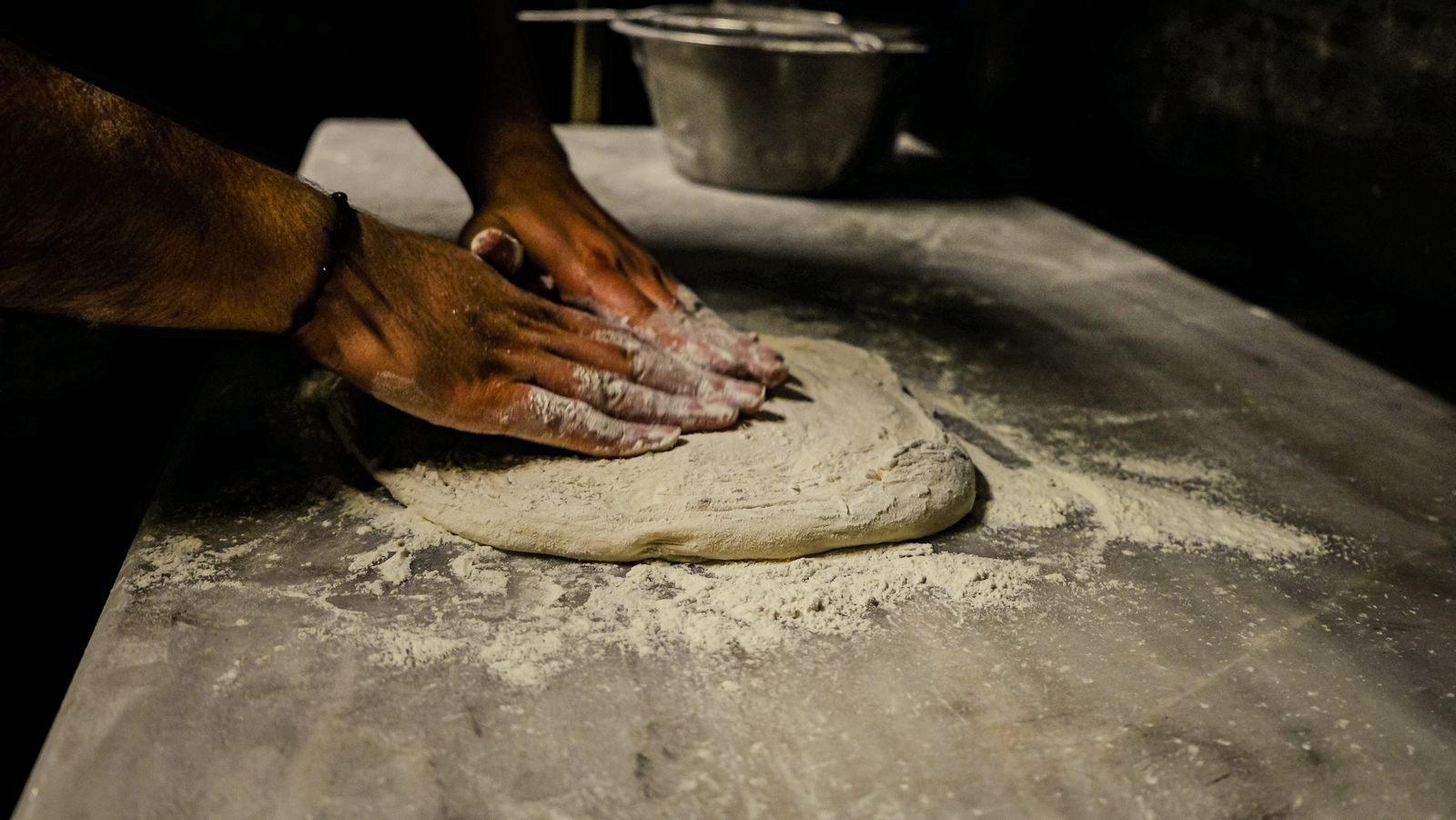 A person kneading pizza dough by hand on a floured surface
