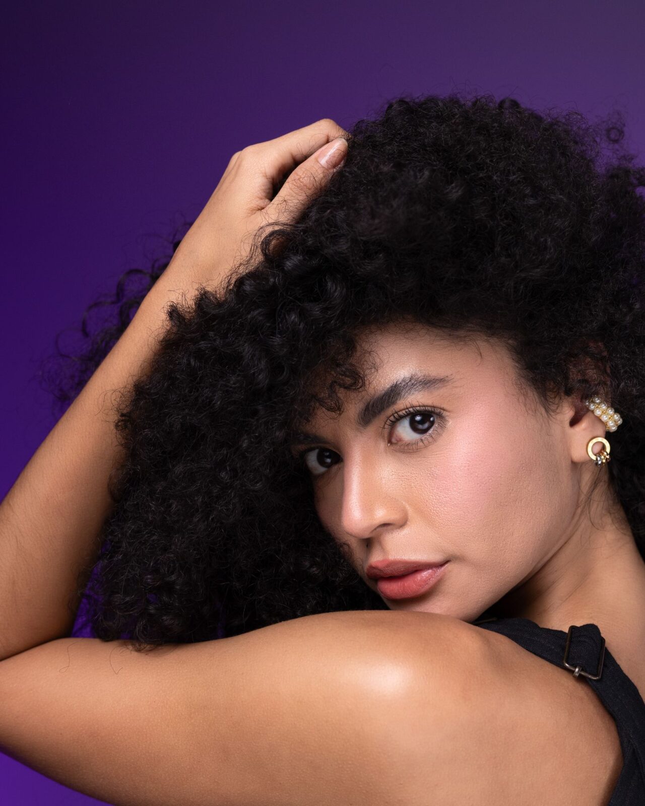 Woman with voluminous natural curly, coily hair styled and glossy against a purple studio background