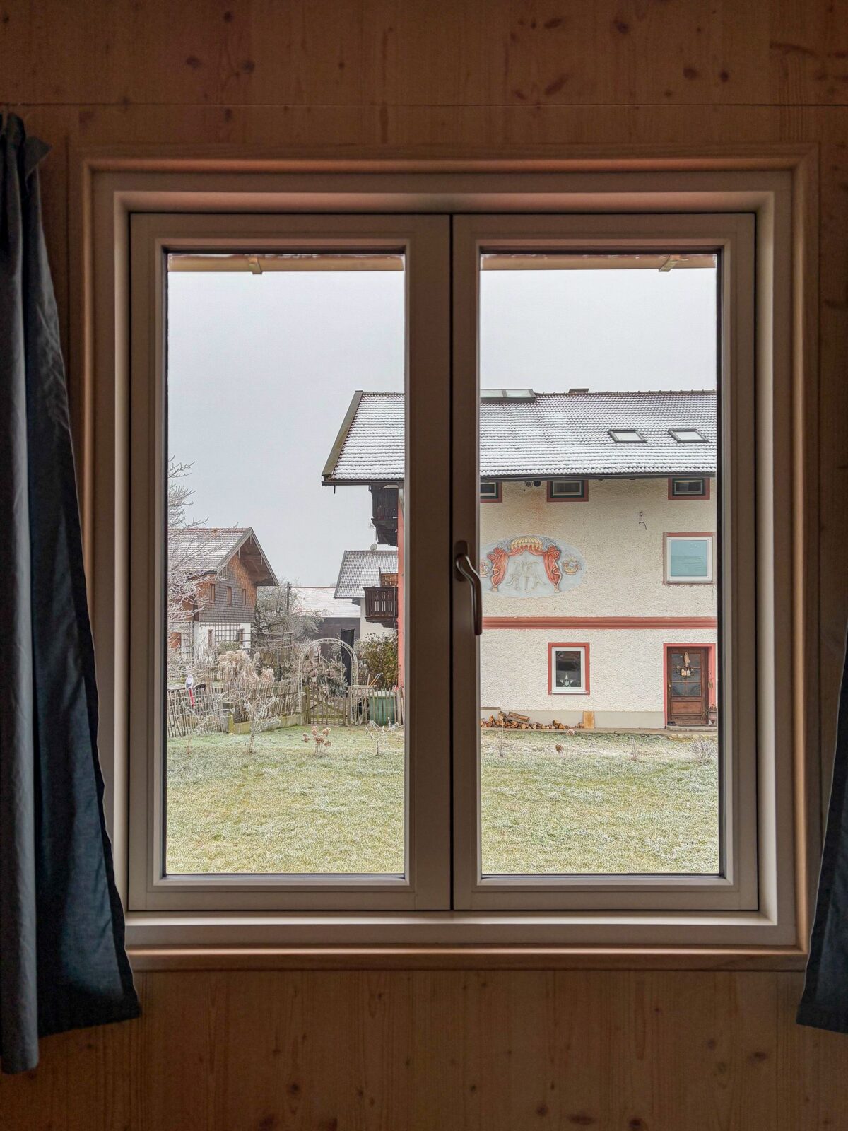 View through an indoor window looking out at snow-dusted houses, showing the type of cold glass surface where window insulation film helps most