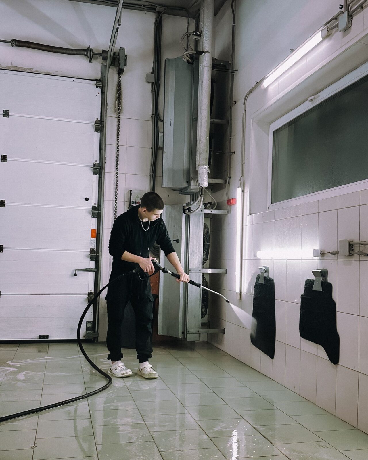 Person pressure washing floor mats in a garage