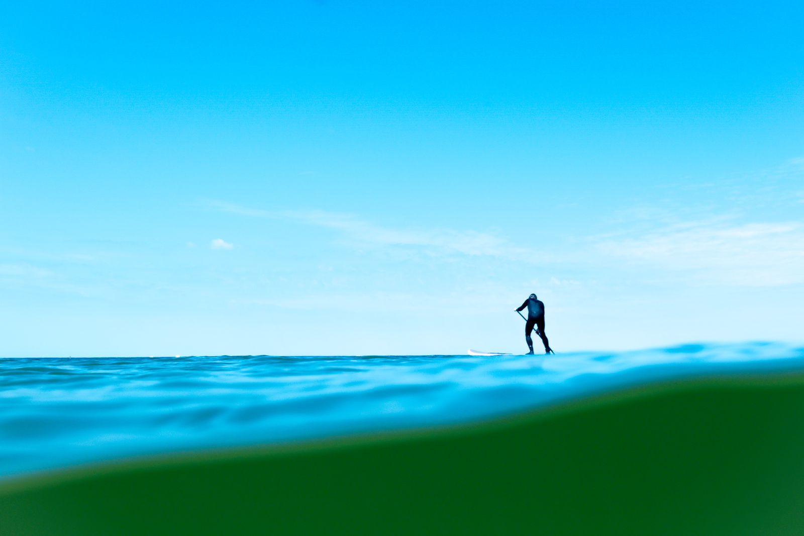 A paddle boarder standing on a board on open water, photographed from the waterline