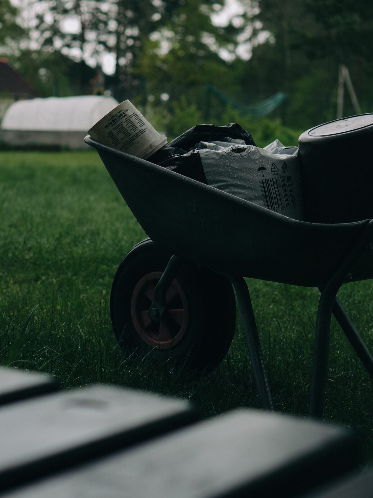 A wheelbarrow loaded with gardening tools sitting on a grassy lawn