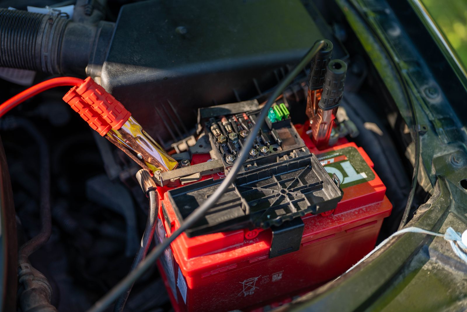 Jumper cables clamped onto a car battery in an engine bay, ready for a jump-start