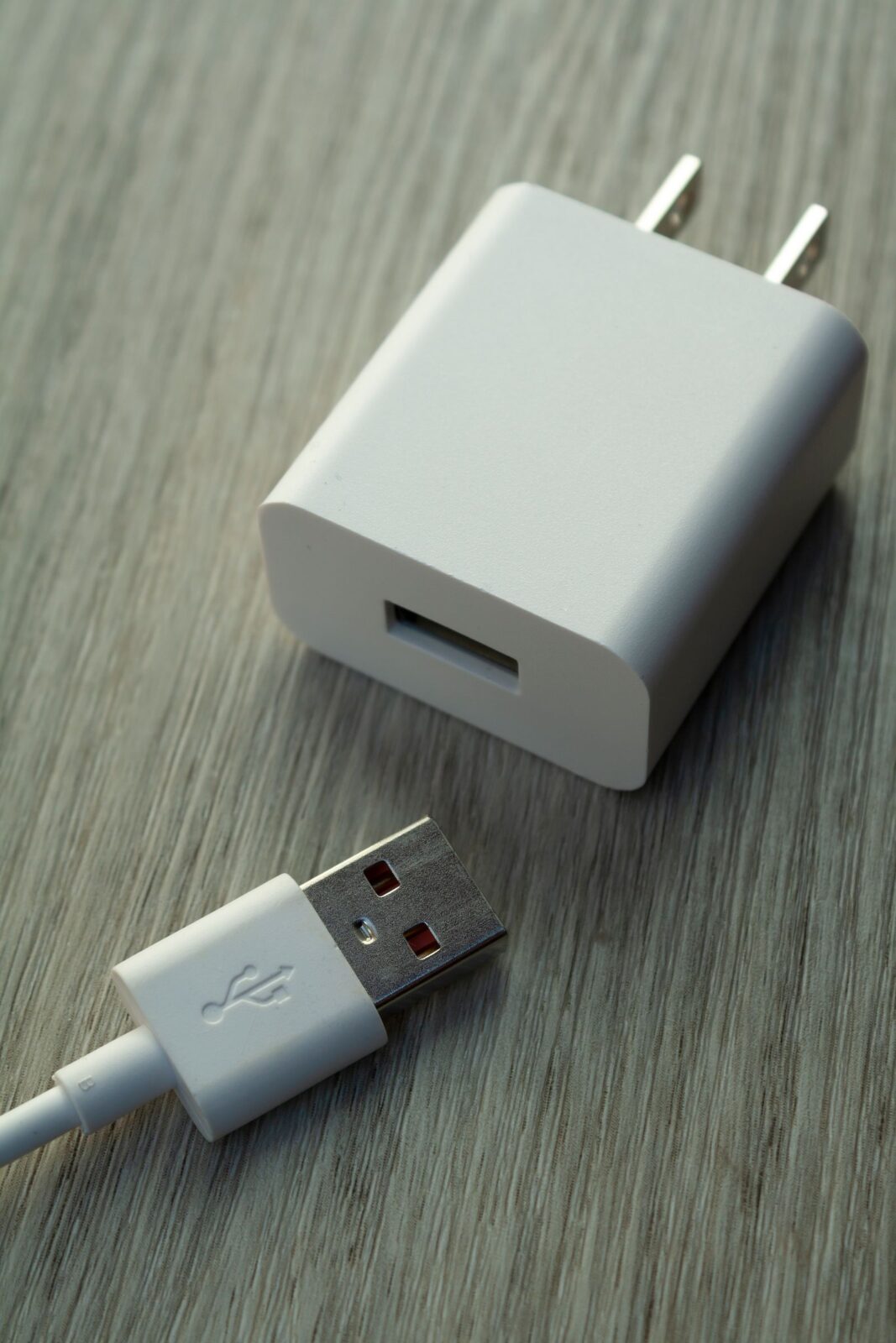 Close-up of a white USB charging cable and adapter resting on a wooden surface