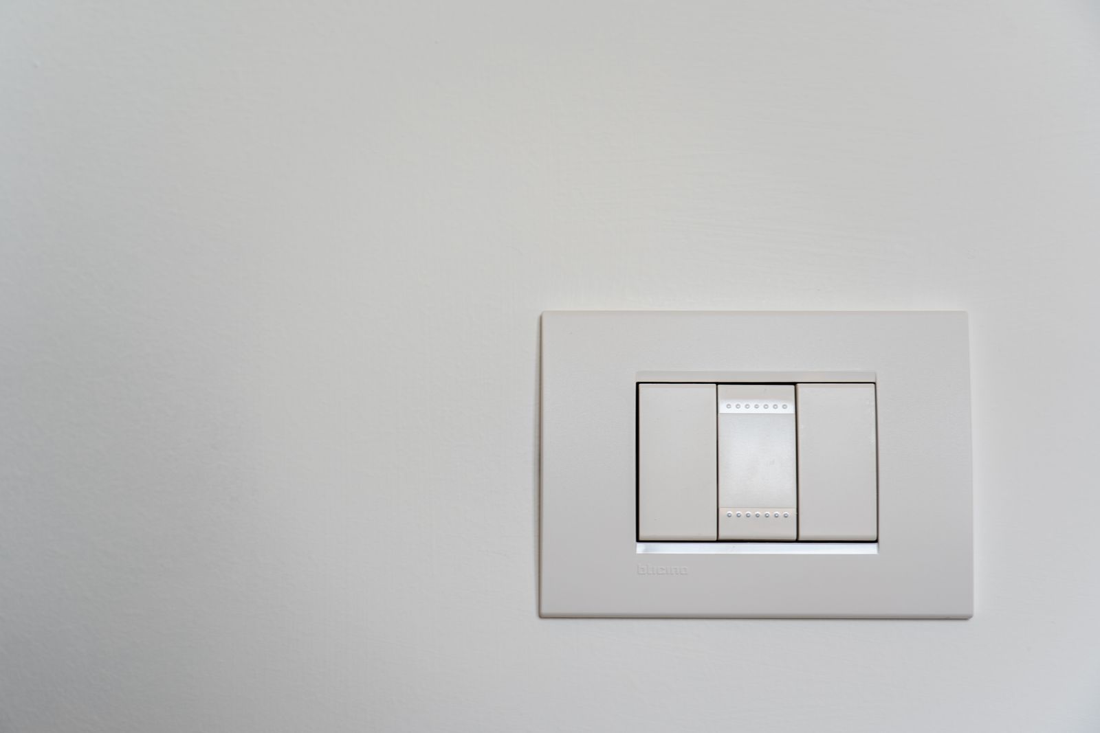Close-up of a white light switch plate mounted on a plain white wall, the type of exterior-wall fixture where foam gaskets stop drafts