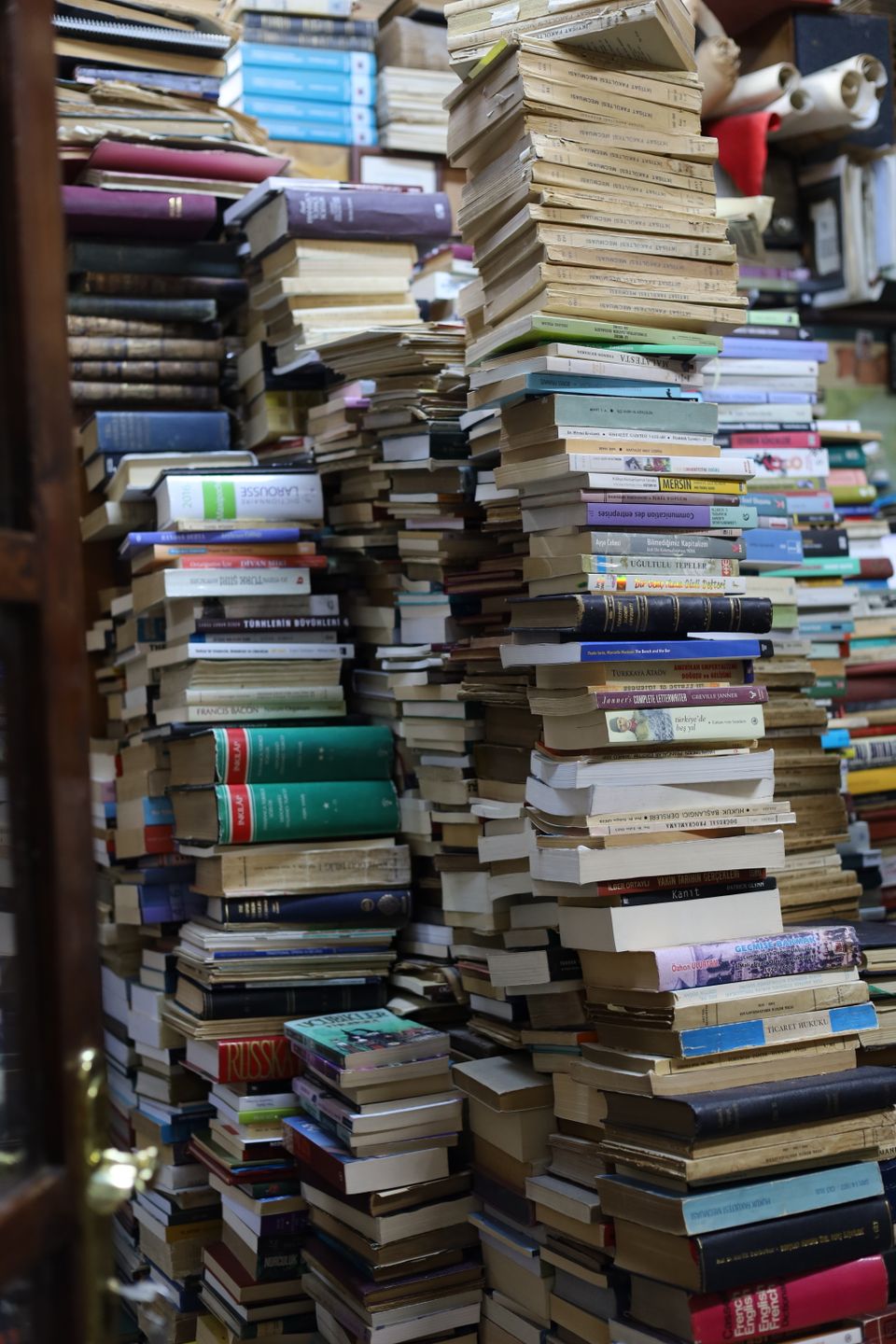 Tall, colorful stacks of books arranged throughout a cluttered, cozy bookstore