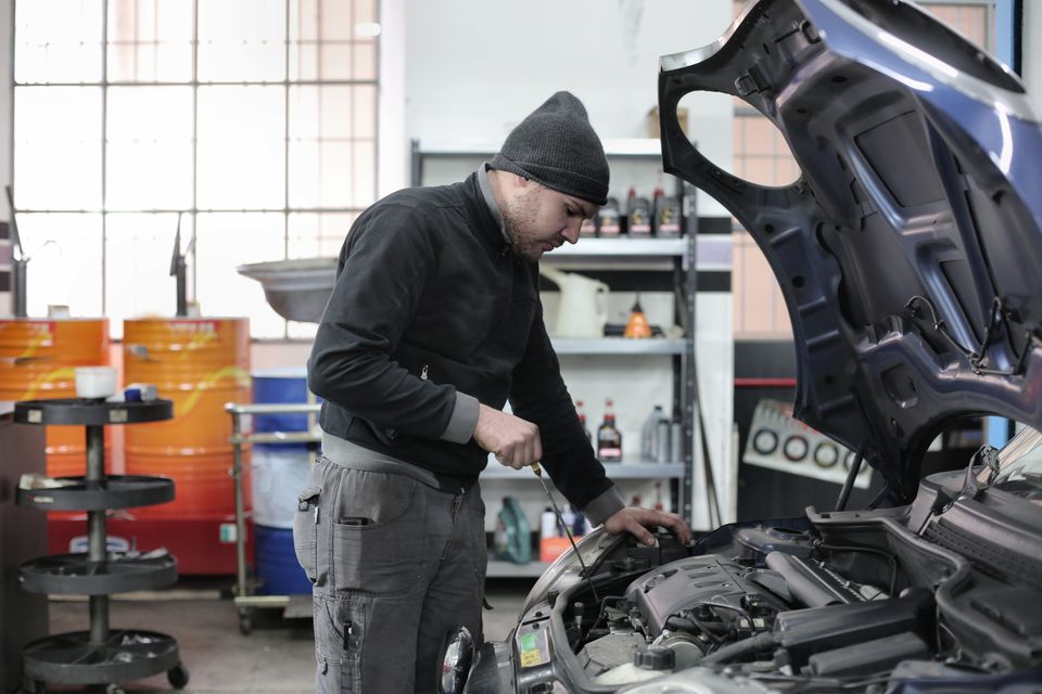 Person inspecting an open car engine bay in a garage, checking connections before hooking up a battery maintainer