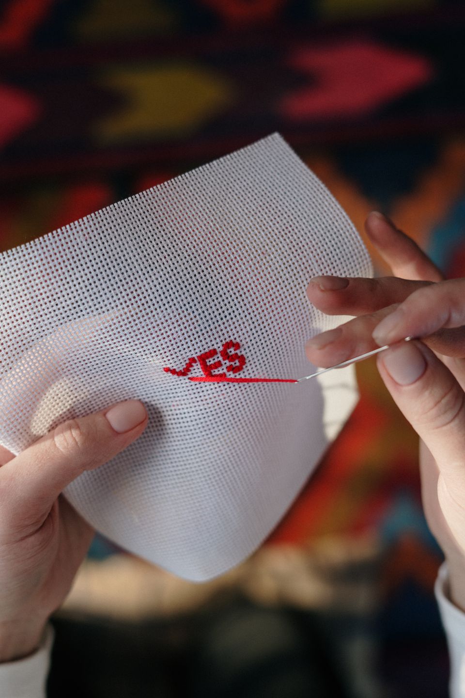 Hands stitching an embroidery hoop with colorful thread on white fabric